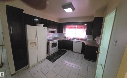 The kitchen features dark wood cabinetry, white appliances, and tiled flooring - 16912 110 Street, Edmonton, AB - Indoor Photo Showing Kitchen