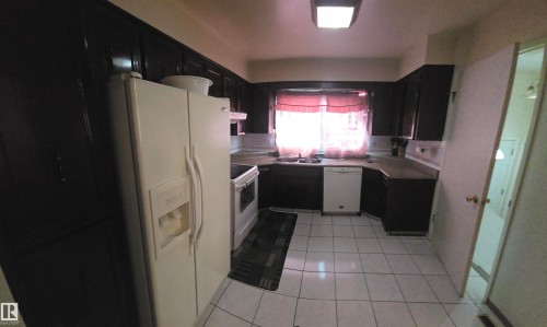 The kitchen features dark cabinetry, white tile flooring, and a white refrigerator with an ice and water dispenser - 16912 110 Street, Edmonton, AB - Indoor Photo Showing Kitchen