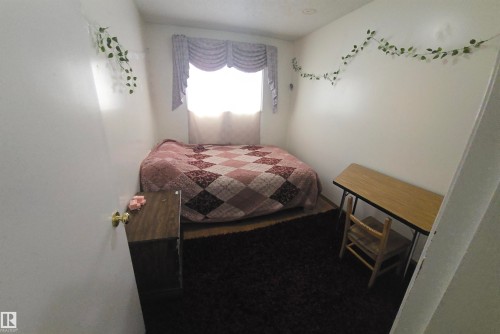 This room features a window with decorative valance, a textured dark rug, and light-colored walls - 16912 110 Street, Edmonton, AB - Indoor Photo Showing Bedroom