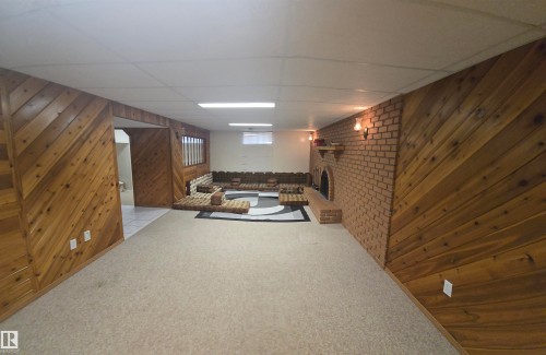 This spacious room features wood paneling, a brick accent wall with an integrated fireplace, and recessed lighting - 16912 110 Street, Edmonton, AB - Indoor