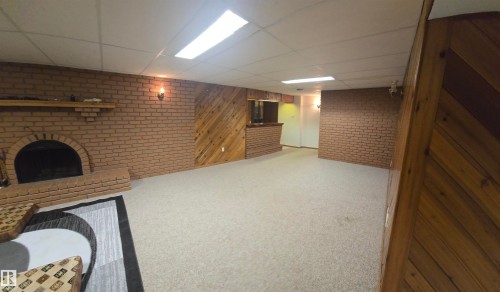 Expansive room featuring brick wall accents, a built-in fireplace, wall-mounted light fixtures, and a recessed ceiling with overhead lighting - 16912 110 Street, Edmonton, AB - Indoor Photo Showing Other Room With Fireplace