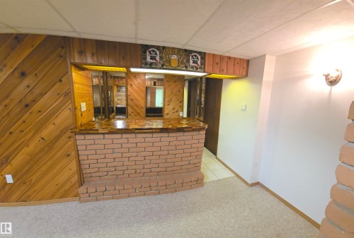 The property features a built-in brick bar with a wood top and mirrored backsplash, and wood-paneled walls - 16912 110 Street, Edmonton, AB - Indoor