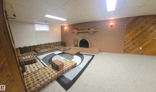 The property features a spacious room with a brick fireplace, a built-in mantel, and a wall accented with diagonal wood paneling - 16912 110 Street, Edmonton, AB - Indoor