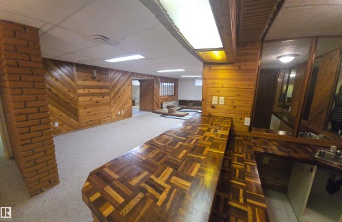 The property features a spacious room with light-colored carpet, wood-paneled walls, and a brick column - 16912 110 Street, Edmonton, AB - Indoor