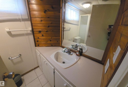 The bathroom features a vanity with a white countertop and sink, a large wall mirror, and wood paneling on one wall - 16912 110 Street, Edmonton, AB - Indoor Photo Showing Bathroom
