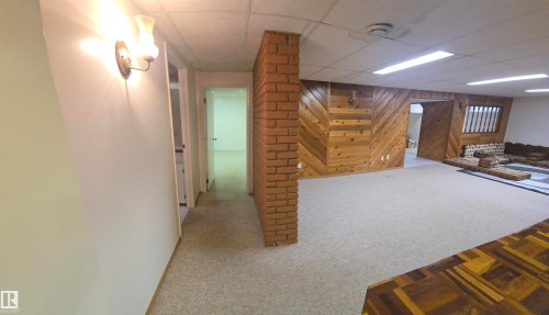The property features a spacious room with light-colored carpeting, brick accents, and wood paneling - 16912 110 Street, Edmonton, AB - Indoor