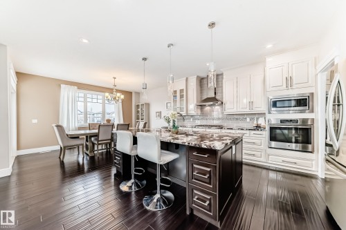 Expansive kitchen featuring a large island with a stone countertop, stainless steel appliances, and sleek white cabinetry - 4134 Charles Link, Edmonton, AB - Indoor