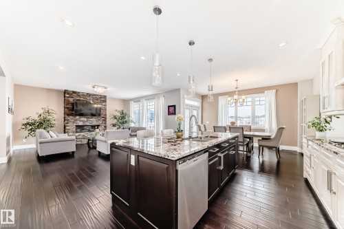 This spacious open-concept living area features rich hardwood flooring, a kitchen island with granite countertops, and a stone-faced fireplace - 4134 Charles Link, Edmonton, AB - Indoor Photo Showing Kitchen With Upgraded Kitchen