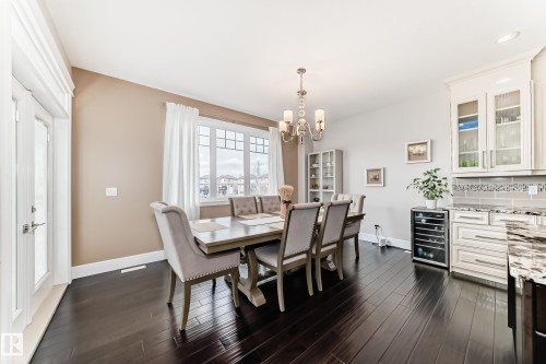 This dining area features dark hardwood flooring, a large window with white trim, and a chandelier - 4134 Charles Link, Edmonton, AB - Indoor Photo Showing Dining Room