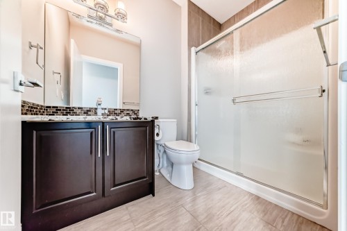 Bathroom featuring a dark wood vanity with a white countertop and a mosaic tile backsplash, a toilet, and a stand-up shower with a glass enclosure - 4134 Charles Link, Edmonton, AB - Indoor Photo Showing Bathroom