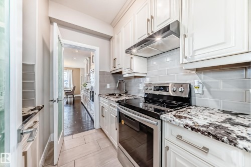 The kitchen features white cabinetry, a stainless steel electric stove, and granite countertops - 4134 Charles Link, Edmonton, AB - Indoor Photo Showing Kitchen With Upgraded Kitchen