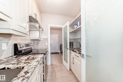 The kitchen features granite countertops, white cabinetry, a stainless steel range hood, and a built-in pantry with frosted glass doors - 4134 Charles Link, Edmonton, AB - Indoor Photo Showing Kitchen