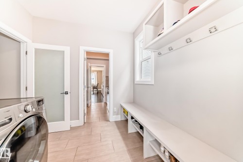 This functional space features a laundry machine, built-in shelving with coat hooks, and a bench with shoe storage below, all illuminated by natural light from a window - 4134 Charles Link, Edmonton, AB - Indoor Photo Showing Laundry Room