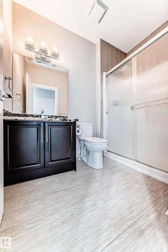 Bathroom featuring a dark wood vanity with a tiled backsplash, a mirrored wall, and a shower with a sliding glass door - 4134 Charles Link, Edmonton, AB - Indoor Photo Showing Bathroom