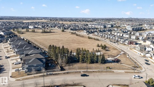 Aerial view of a residential neighbourhood featuring numerous homes with dark roofs, streets, and an undeveloped field with scattered trees - 4134 Charles Link, Edmonton, AB - Outdoor With View