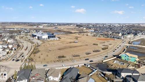 Aerial view showcasing the surrounding neighborhood, including residential properties, a central field area, and commercial buildings - 4134 Charles Link, Edmonton, AB - Outdoor With View