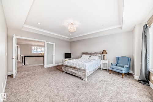 This carpeted room features a tray ceiling with recessed lighting and a decorative chandelier - 4134 Charles Link, Edmonton, AB - Indoor Photo Showing Bedroom