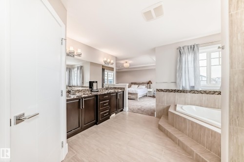 The property features a bathroom with light-colored floor tiles, a built-in bathtub with tiled surround, and a vanity with dark wood cabinetry and a stone countertop - 4134 Charles Link, Edmonton, AB - Indoor Photo Showing Bathroom