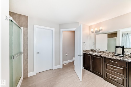 The bathroom features a dual sink vanity with a granite countertop, a glass-enclosed shower, and tiled flooring - 4134 Charles Link, Edmonton, AB - Indoor Photo Showing Other Room