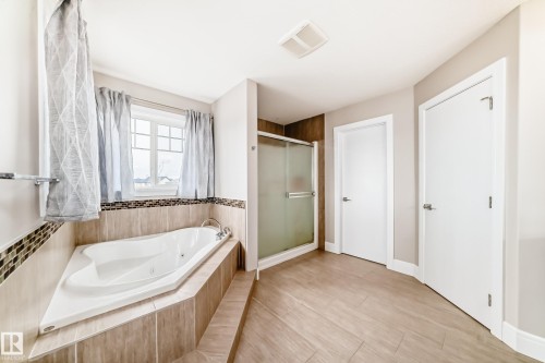 Bathroom featuring a corner soaking tub with tile surround, a glass-enclosed shower, and light-colored flooring - 4134 Charles Link, Edmonton, AB - Indoor Photo Showing Bathroom