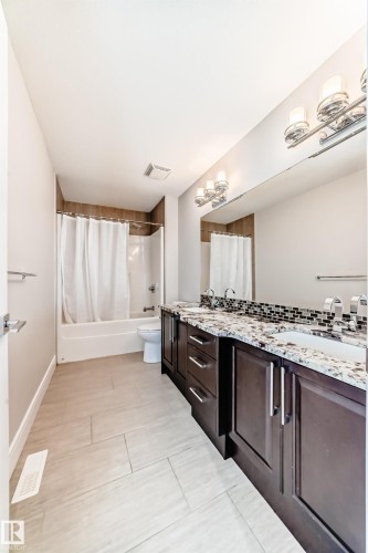 Bathroom featuring a double vanity with granite countertops, dark wood cabinetry, two sinks, and a large mirror with sconce lighting - 4134 Charles Link, Edmonton, AB - Indoor
