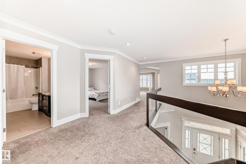This property features a light-filled corridor with neutral carpeting, a modern chandelier, and a view into a bathroom with a tub and vanity, as well as a separate room - 4134 Charles Link, Edmonton, AB - Indoor Photo Showing Other Room