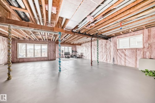 The unfinished basement features exposed wood ceiling joists and support beams, large windows, and a concrete floor - 4134 Charles Link, Edmonton, AB - Indoor Photo Showing Basement