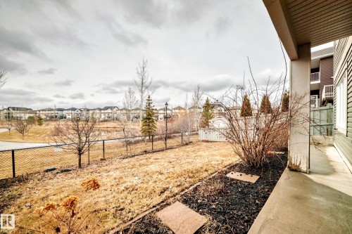 The property features a concrete patio and a sloped yard with a fence, overlooking a pond and residential properties in the background - 4134 Charles Link, Edmonton, AB - Outdoor