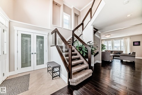 Entryway featuring dark hardwood flooring, a carpeted staircase with wood and glass railing, and double doors with frosted glass panels - 4134 Charles Link, Edmonton, AB - Indoor Photo Showing Other Room