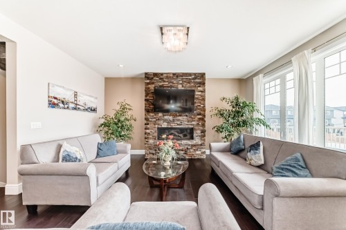 Living room featuring dark hardwood floors, a stone-clad fireplace, and large windows providing natural light - 4134 Charles Link, Edmonton, AB - Indoor Photo Showing Living Room With Fireplace