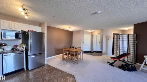 The open-concept living area features a kitchen with stainless steel appliances and white cabinetry, a dining area with a wooden table, and a carpeted space - 1318 330 Clareview Station Drive Nw, Edmonton, AB - Indoor