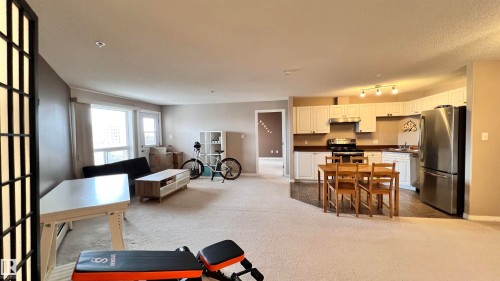 The property features an open-concept living area with carpeted floors, a kitchen with white cabinetry and stainless steel appliances, and large windows that provide natural light - 1318 330 Clareview Station Drive Nw, Edmonton, AB - Indoor