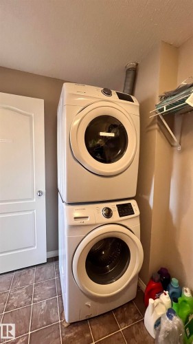 The laundry area features a stacked washer and dryer, tile flooring, and a wall-mounted shelf - 1318 330 Clareview Station Drive Nw, Edmonton, AB - Indoor Photo Showing Laundry Room