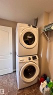 The laundry area features a stacked washer and dryer, tile flooring, and a wall-mounted shelf - 