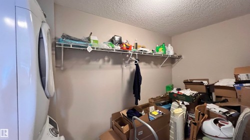 This utility area features a white stacked washer and dryer unit, a wall-mounted wire shelf, and a clothing rod - 1318 330 Clareview Station Drive Nw, Edmonton, AB - Indoor