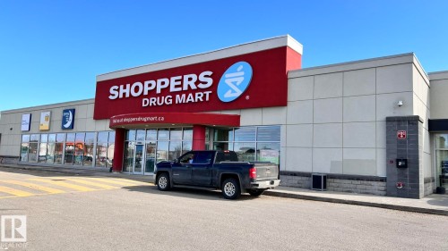 Commercial building featuring a prominent storefront with large windows, a red awning, and a spacious paved parking lot - 1318 330 Clareview Station Drive Nw, Edmonton, AB - Outdoor