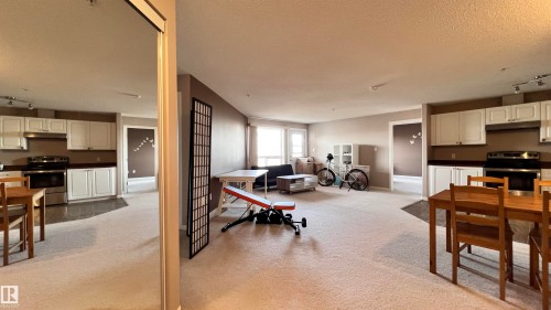 Spacious living area featuring light-colored carpeting, white kitchen cabinetry with dark countertops, and stainless steel appliances - 1318 330 Clareview Station Drive Nw, Edmonton, AB - Indoor