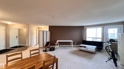 This open-plan living area features light-colored carpeting and a feature wall with a contrasting brown paint finish - 1318 330 Clareview Station Drive Nw, Edmonton, AB - Indoor