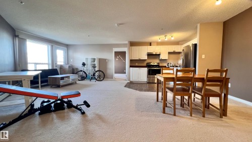 Expansive open-concept living space featuring light-colored carpeting, a kitchen with light cabinetry and stainless steel appliances, and a dining area with wooden furniture - 1318 330 Clareview Station Drive Nw, Edmonton, AB - Indoor