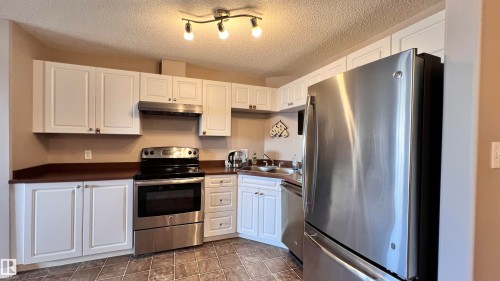Kitchen featuring white cabinetry, dark countertops, stainless steel appliances, and tiled flooring - 1318 330 Clareview Station Drive Nw, Edmonton, AB - Indoor Photo Showing Kitchen