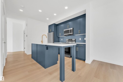 The kitchen features blue cabinetry, stainless steel appliances, a white island with a gold-toned faucet, and recessed lighting - 57 710 Mattson Drive, Edmonton, AB - Indoor Photo Showing Kitchen With Upgraded Kitchen
