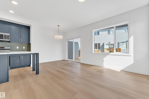 The open concept living area features light-toned flooring, a kitchen with blue cabinetry and stainless steel appliances, and a sliding glass door leading to an outdoor space - 57 710 Mattson Drive, Edmonton, AB - Indoor Photo Showing Kitchen