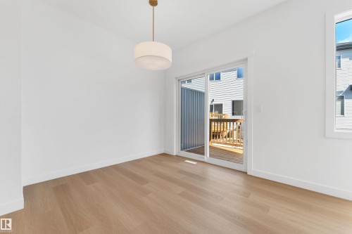 This versatile room features light hardwood flooring, a modern drum pendant light fixture, and a sliding glass door that provides access to an outdoor deck - 57 710 Mattson Drive, Edmonton, AB - Indoor Photo Showing Other Room