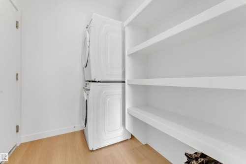 Laundry area featuring a stackable washer and dryer, built-in shelving, and light wood flooring - 57 710 Mattson Drive, Edmonton, AB - Indoor