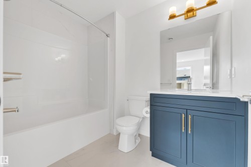 The bathroom features a deep blue vanity with gold-toned hardware, a white countertop, and a vanity mirror illuminated by a modern light fixture - 57 710 Mattson Drive, Edmonton, AB - Indoor Photo Showing Bathroom