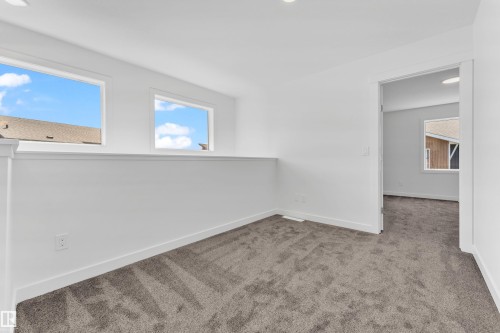 This open space features light gray carpeting, white walls, and two windows providing natural light - 57 710 Mattson Drive, Edmonton, AB - Indoor Photo Showing Other Room