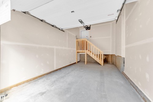 The garage features a concrete floor, light-colored walls, and a wooden stairway providing access to another area - 57 710 Mattson Drive, Edmonton, AB - Indoor