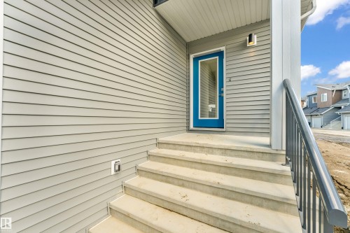 The property features light gray siding, a bright blue entrance door with a window, and concrete steps leading to the entrance - 57 710 Mattson Drive, Edmonton, AB - Outdoor With Exterior