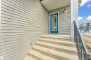 The property features light gray siding, a bright blue entrance door with a window, and concrete steps leading to the entrance - 57 710 Mattson Drive, Edmonton, AB  - Outdoor With Exterior 