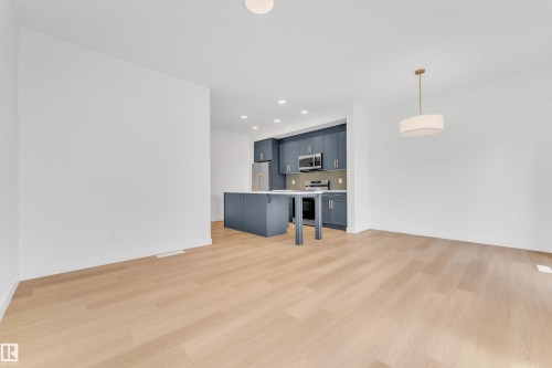 Spacious open-concept living area featuring light-toned hardwood flooring and a modern kitchen with blue cabinetry, stainless steel appliances, and a central island - 57 710 Mattson Drive, Edmonton, AB - Indoor Photo Showing Kitchen